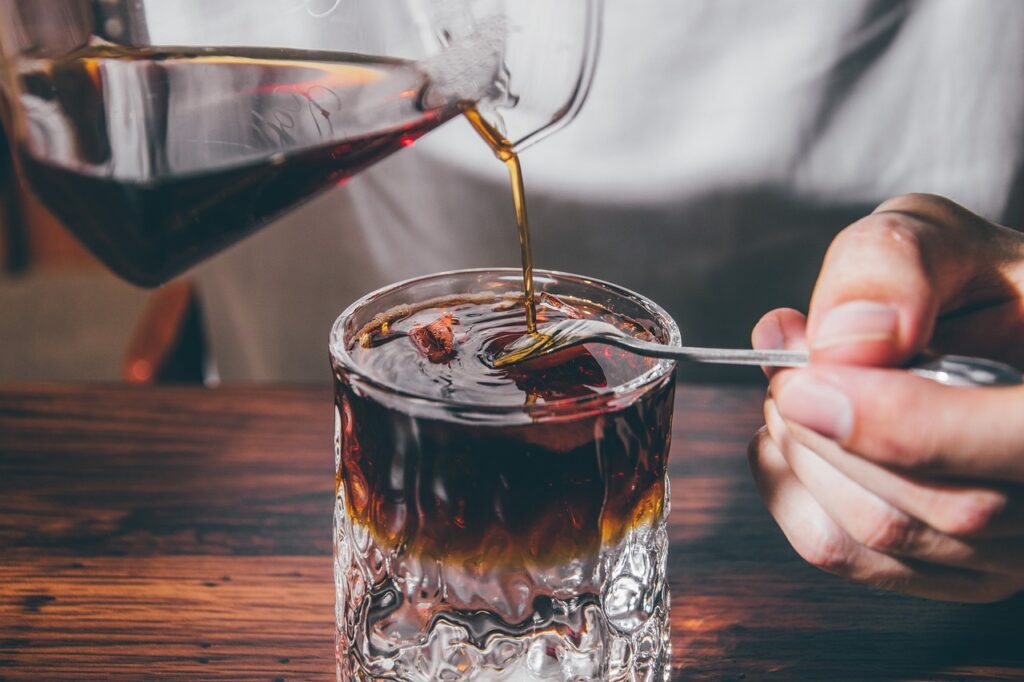 Jemand gießt Cold Brew in ein Glas mit Eiswürfeln